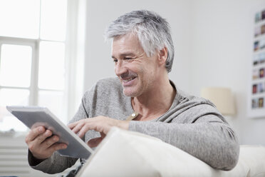 Deutschland, Bayern, München, Älterer Mann mit digitalem Tablet auf Couch, lächelnd - RBF001267