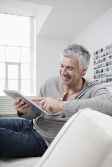 Deutschland, Bayern, München, Älterer Mann mit digitalem Tablet auf Couch, lächelnd - RBF001268