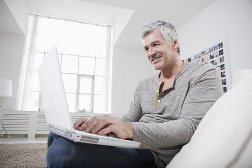 Deutschland, Bayern, München, Älterer Mann mit Laptop auf Couch, lächelnd - RBF001270