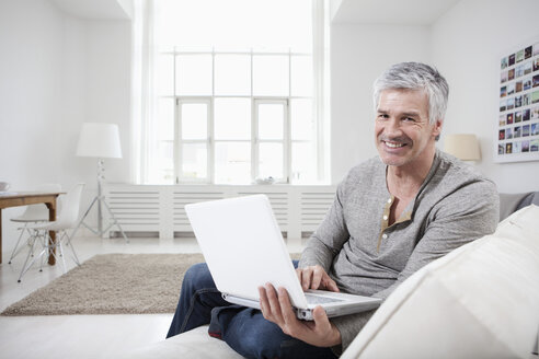 Deutschland, Bayern, München, Porträt eines reifen Mannes mit Laptop auf der Couch, lächelnd - RBF001271