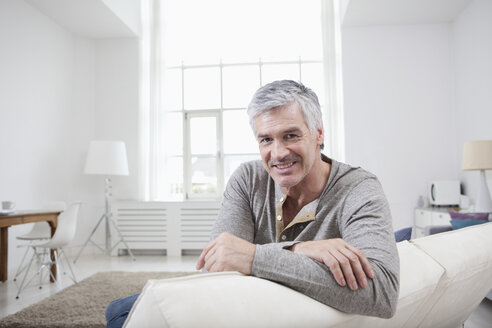 Deutschland, Bayern, München, Porträt eines reifen Mannes auf einer Couch sitzend, lächelnd - RBF001207
