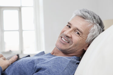 Germany, Bavaria, Munich, Portrait of mature man relaxing on sofa, smiling - RBF001212