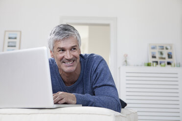 Deutschland, Bayern, München, Älterer Mann mit Laptop auf Couch, lächelnd - RBF001273