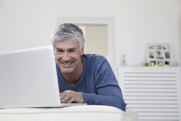 Deutschland, Bayern, München, Porträt eines reifen Mannes mit Laptop auf der Couch, lächelnd - RBF001274