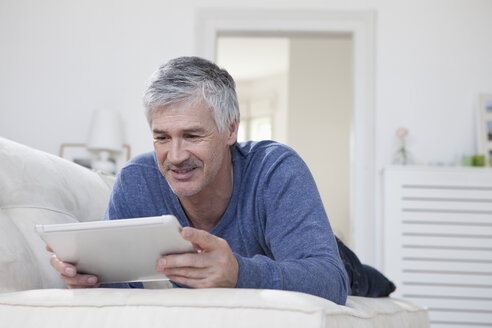 Deutschland, Bayern, München, Älterer Mann mit digitalem Tablet auf Couch, lächelnd - RBF001275