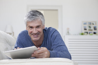 Deutschland, Bayern, München, Porträt eines reifen Mannes mit digitalem Tablet auf der Couch, lächelnd - RBF001264
