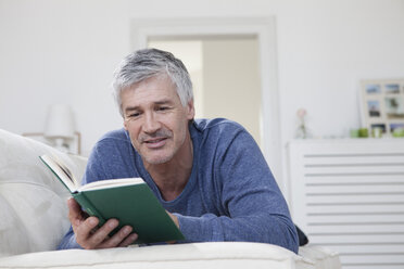 Germany, Bavaria, Munich, Mature man reading book on couch, smiling - RBF001276