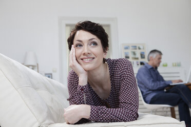 Germany, Bavaria, Munich, Woman leaning on sofa while man using laptop in background - RBF001224