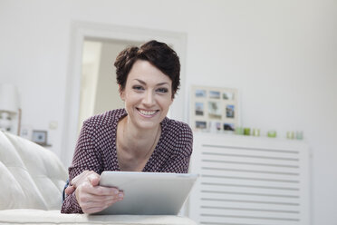 Germany, Bavaria, Munich, Portrait of mid adult woman using digital tablet on couch, smiling - RBF001203