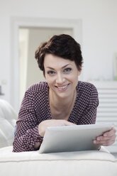 Germany, Bavaria, Munich, Portrait of mid adult woman using digital tablet on couch, smiling - RBF001201