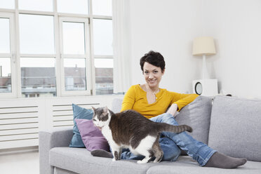 Deutschland, Bayern, München, Porträt einer mittleren erwachsenen Frau mit Katze auf der Couch, lächelnd - RBF001256
