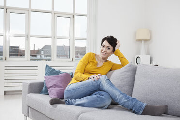 Germany, Bavaria, Munich, Portrait of mid adult woman sitting on couch, smiling - RBF001314