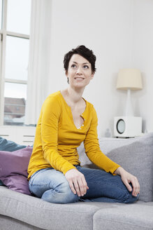 Deutschland, Bayern, München, Mid erwachsene Frau sitzt auf Couch, lächelnd - RBF001243