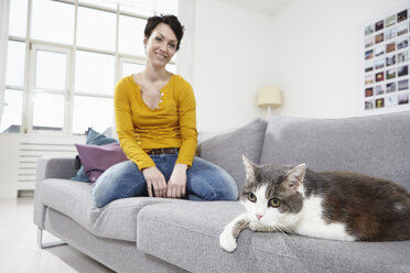 Germany, Bavaria, Munich, Mid adult woman with cat on couch, smiling - RBF001303