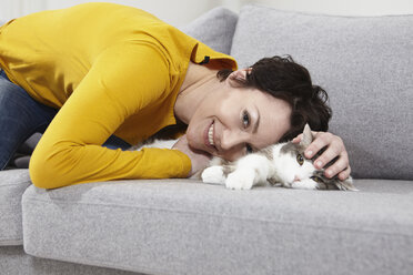 Deutschland, Bayern, München, Mittlere erwachsene Frau mit Katze auf Couch, lächelnd - RBF001302