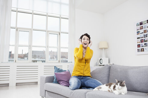 Deutschland, Bayern, München, Mittlere erwachsene Frau hört Musik mit Katze auf Couch - RBF001244