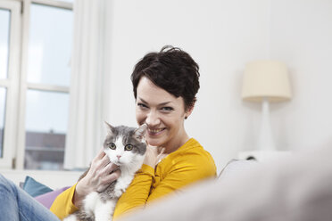 Germany, Bavaria, Munich, Portrait of mid adult woman with cat on couch, smiling - RBF001298