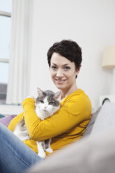 Germany, Bavaria, Munich, Portrait of mid adult woman with cat on couch, smiling - RBF001197