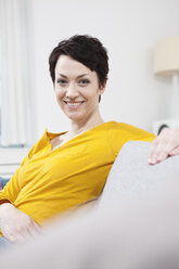 Germany, Bavaria, Munich, Portrait of mid adult woman sitting on couch, smiling - RBF001199