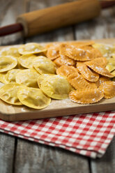Variety of ravioli filled with tomato, ham and mushrooms on chopping board - MAEF006384