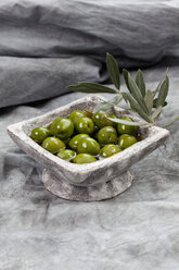 Bowl of green olives in olive oil on textile, close up - CSF018506