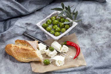 Sheep's cheese with green olives in olive oil, chili and white bread on textile, close up - CSF018477