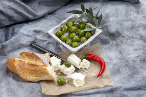 Schafskäse mit grünen Oliven in Olivenöl, Chili und Weißbrot auf Textil, Nahaufnahme - CSF018477