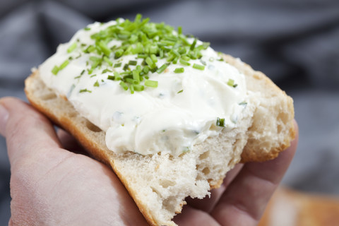 Menschliche Hand hält Brot mit Frischkäse, Schnittlauch, Nahaufnahme, lizenzfreies Stockfoto