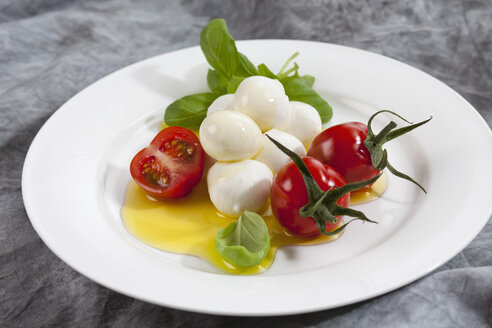 Mozzarella-Käsekugeln, Tomaten, Olivenöl und Basilikumkraut auf einem Teller, Nahaufnahme - CSF018529