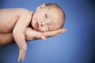 Newborn baby lying on fathers arm against blue background, close up - MFF000529