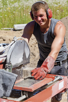 Germany, Rhineland Palatinate, Young man cutting paving stone with saw - CSF018824