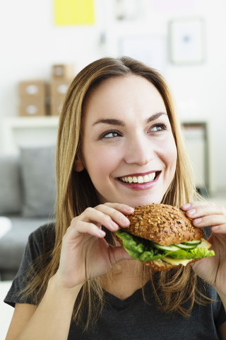 Germany, Bavaria, Munich, Young woman holding sandwich, looking away stock photo