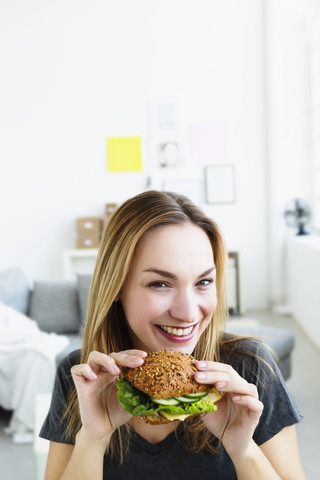 Deutschland, Bayern, München, Porträt einer jungen Frau mit Sandwich in der Hand, lächelnd, lizenzfreies Stockfoto