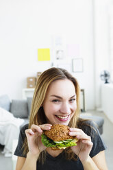 Deutschland, Bayern, München, Porträt einer jungen Frau mit Sandwich in der Hand, lächelnd - SPOF000307