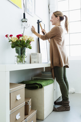 Deutschland, Bayern, München, Junge Frau hämmert an die Wand, lächelnd, lizenzfreies Stockfoto