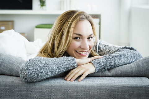 Deutschland, Bayern, München, Porträt einer jungen Frau, die lächelnd auf der Couch liegt, lizenzfreies Stockfoto