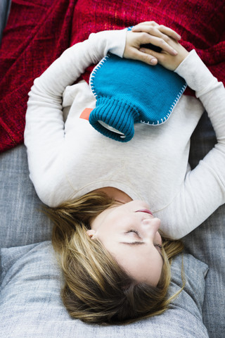 Germany, Bavaria, Munich, Young woman sleeping on couch with hot water bottle stock photo