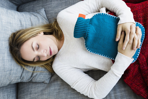 Germany, Bavaria, Munich, Young woman sleeping on couch with hot water bottle stock photo