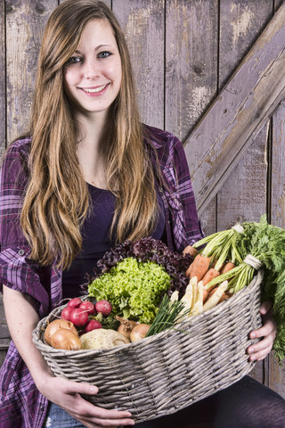 Deutschland, Porträt eines lächelnden Mädchens, das einen Korb mit Biogemüse hält, lizenzfreies Stockfoto