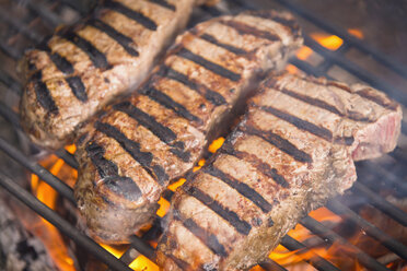 Strip steak grilling on hot barbecue fire, close up - ABAF000821