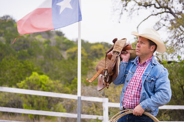 Texas, Älterer Mann mit Cowboyhut, Seil und Sattel vor einer Flagge stehend - ABAF000823