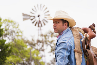 Texas, Cowboy mit Sattel und Ranch-Windmühle im Hintergrund - ABAF000826