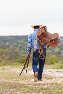 Texas, Cowboy walking with rifle and saddle - ABAF000829