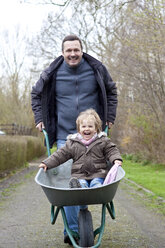 Germany, Father pushing daughter on wheel barrow, smiling - JFEF000085