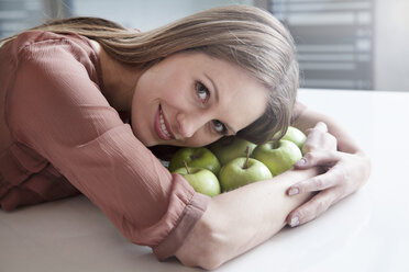 Germany, North Rhine Westphalia, Cologne, Portrait of businesswoman with green apples, smiling - FMKF000731