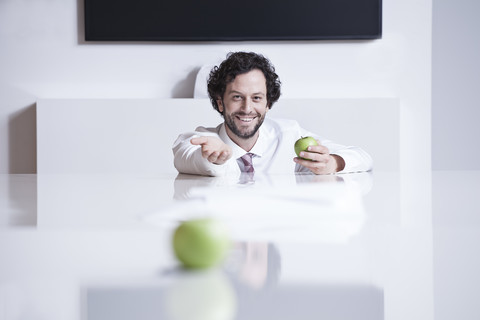Deutschland, Nordrhein-Westfalen, Köln, Porträt eines Geschäftsmannes mit grünem Apfel, lächelnd, lizenzfreies Stockfoto