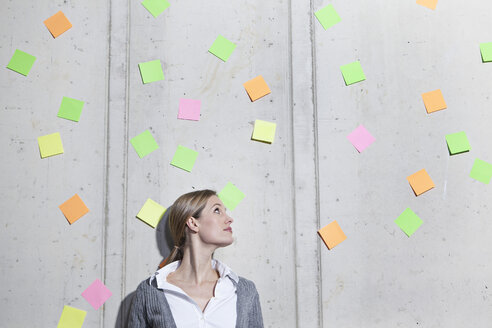 Germany, North Rhine Westphalia, Cologne, Businesswoman looking up at adhesive notes - FMKF000726