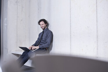 Germany, North Rhine Westphalia, Cologne, Portrait of businessman with laptop, smiling - FMKF000776