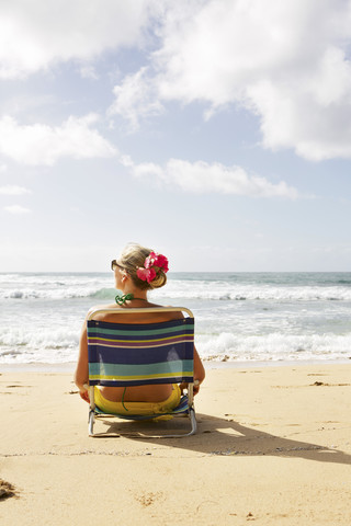 USA, Hawaii, Mittlere erwachsene Frau sitzt auf Liegestuhl am Strand, lizenzfreies Stockfoto