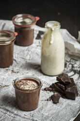 Jars of chocolate pudding with vanilla sauce in bottle on newspaper, close up - SBD000029